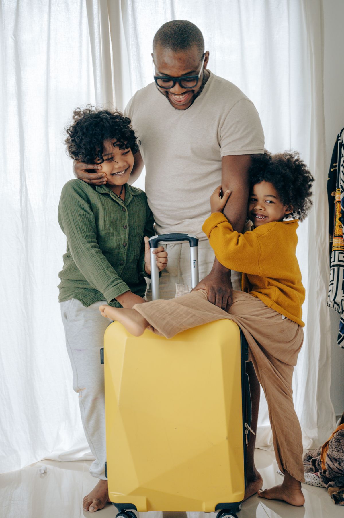 Un père souriant avec ses deux enfants et leur valise, prêts pour le voyage
