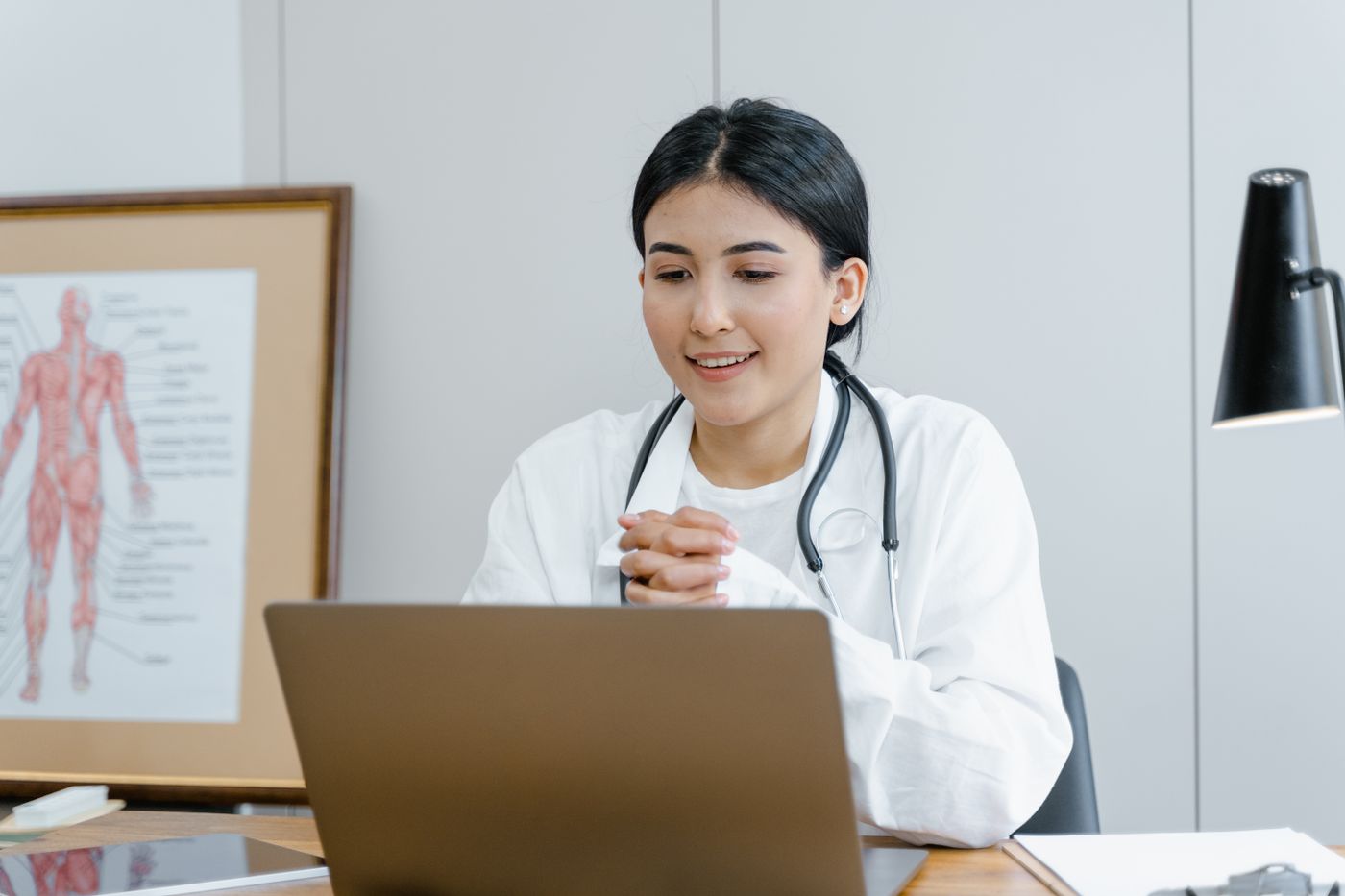Une médecin souriante en consultation vidéo depuis son bureau